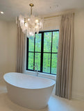Modern bathroom with a freestanding bathtub, chandelier, and large window. 
Elegant floor-length washed linen drapes in oatmeal beige for modern luxury interiors