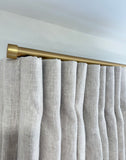 Natural linen curtains with a gold curtain rod against a white wall