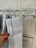Plaid fabric hanging on a metal rod with clips against a neutral wall.