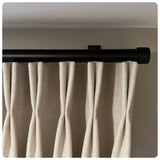 Beige curtains hanging from a black curtain rod against a neutral wall. black designer drapery hardware