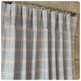 Plaid shower curtain with beige and gray pattern on a metal rod against a neutral background