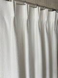 Close-up of a white fabric shower curtain with a metal rod.